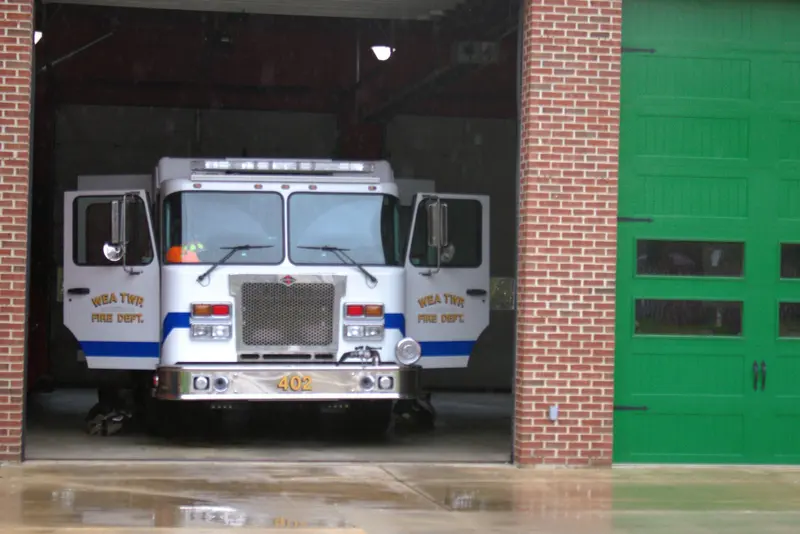 A white fire engine parked in an open bay beside a green bay door.